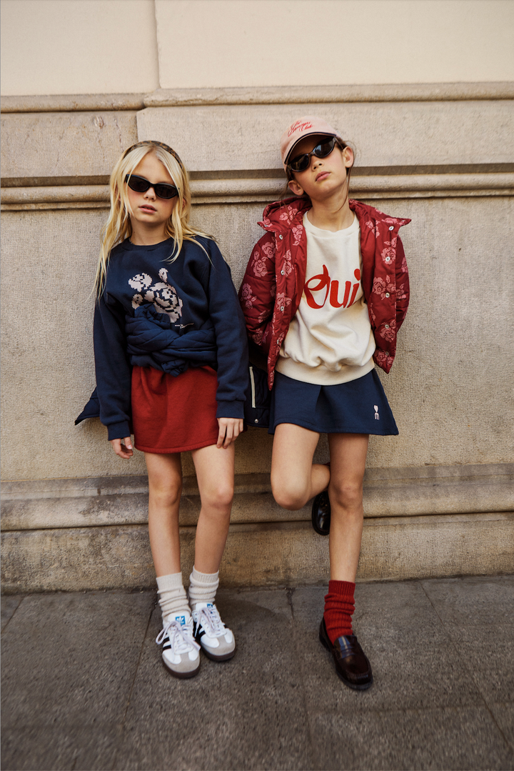 Two children posing against a stone wall, wearing stylish outfits.