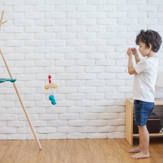 Child playing with toys in a room with a white brick wall and wooden floor.