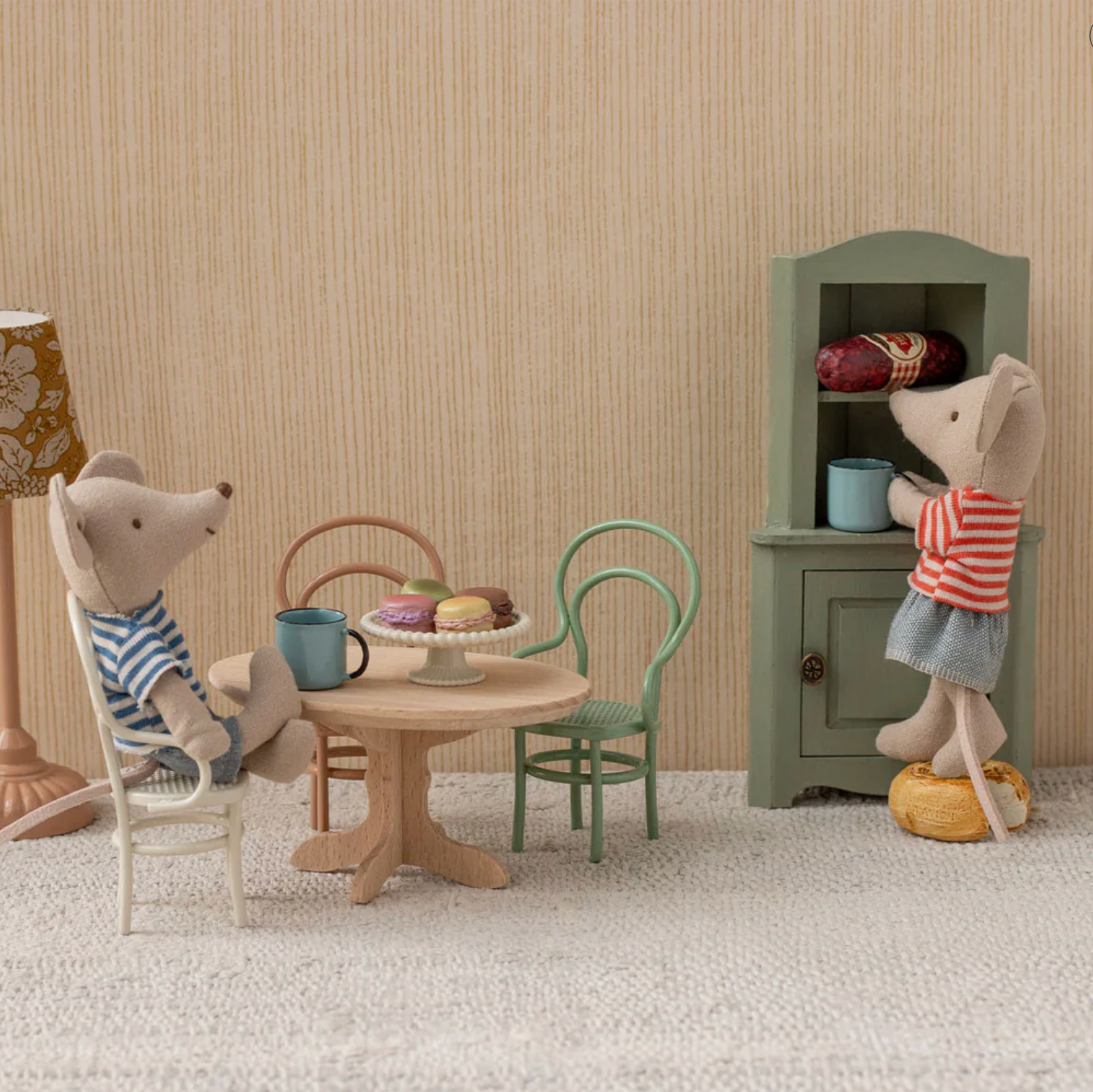 Miniature scene with toy mice around a table and chair, set against a striped wall.