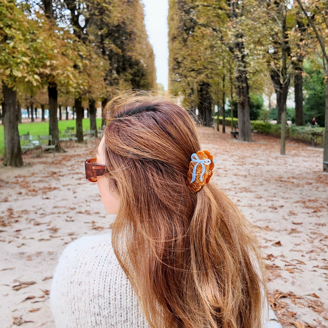 Woman with long hair wearing a decorative hair clip in an outdoor setting with trees and a path.