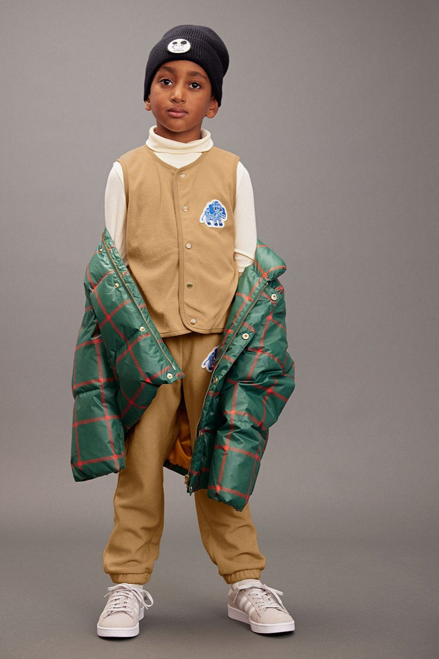 Child wearing a beige vest, plaid jacket, and pants on a gray background