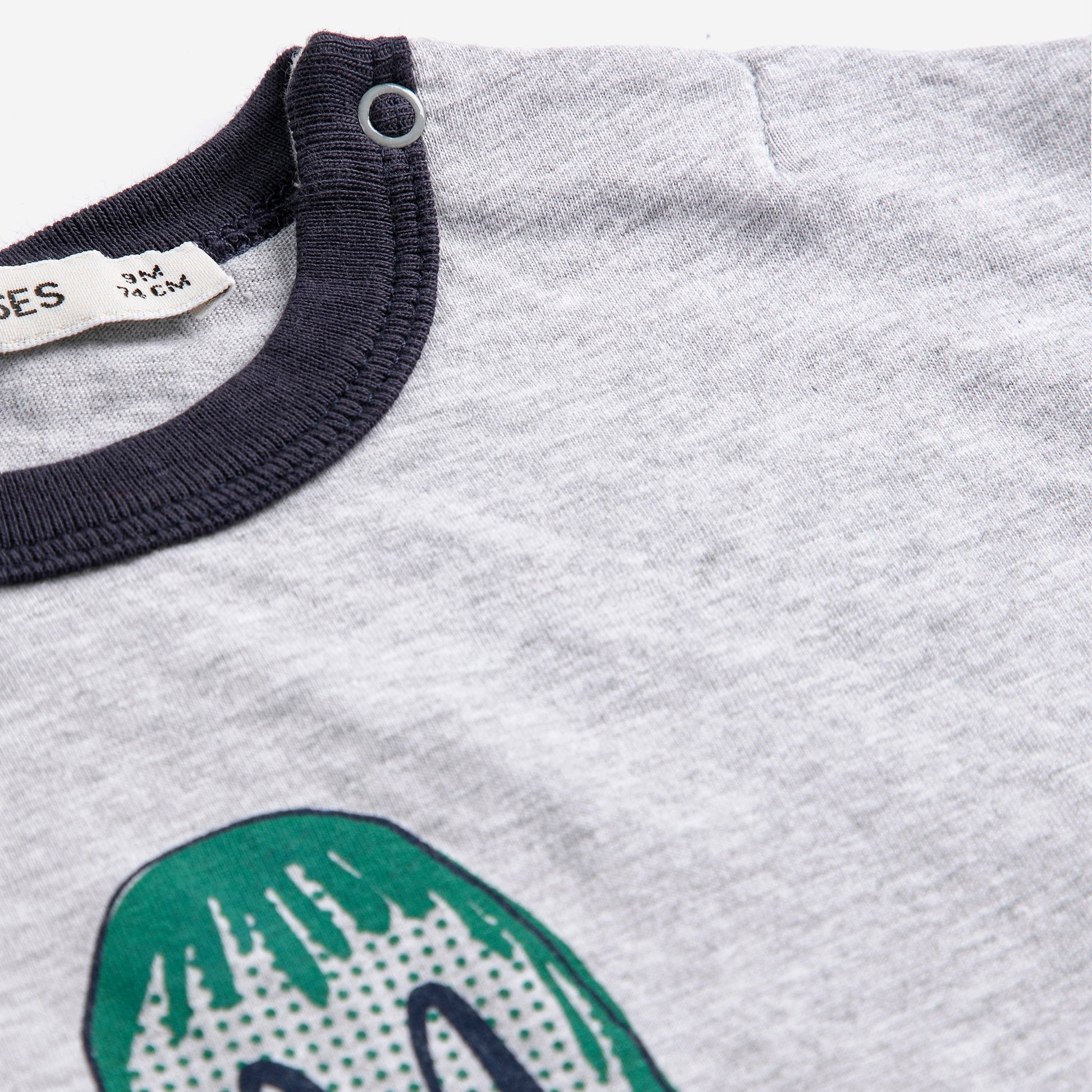 Gray shirt with green dinosaur design and navy collar, brand label visible.