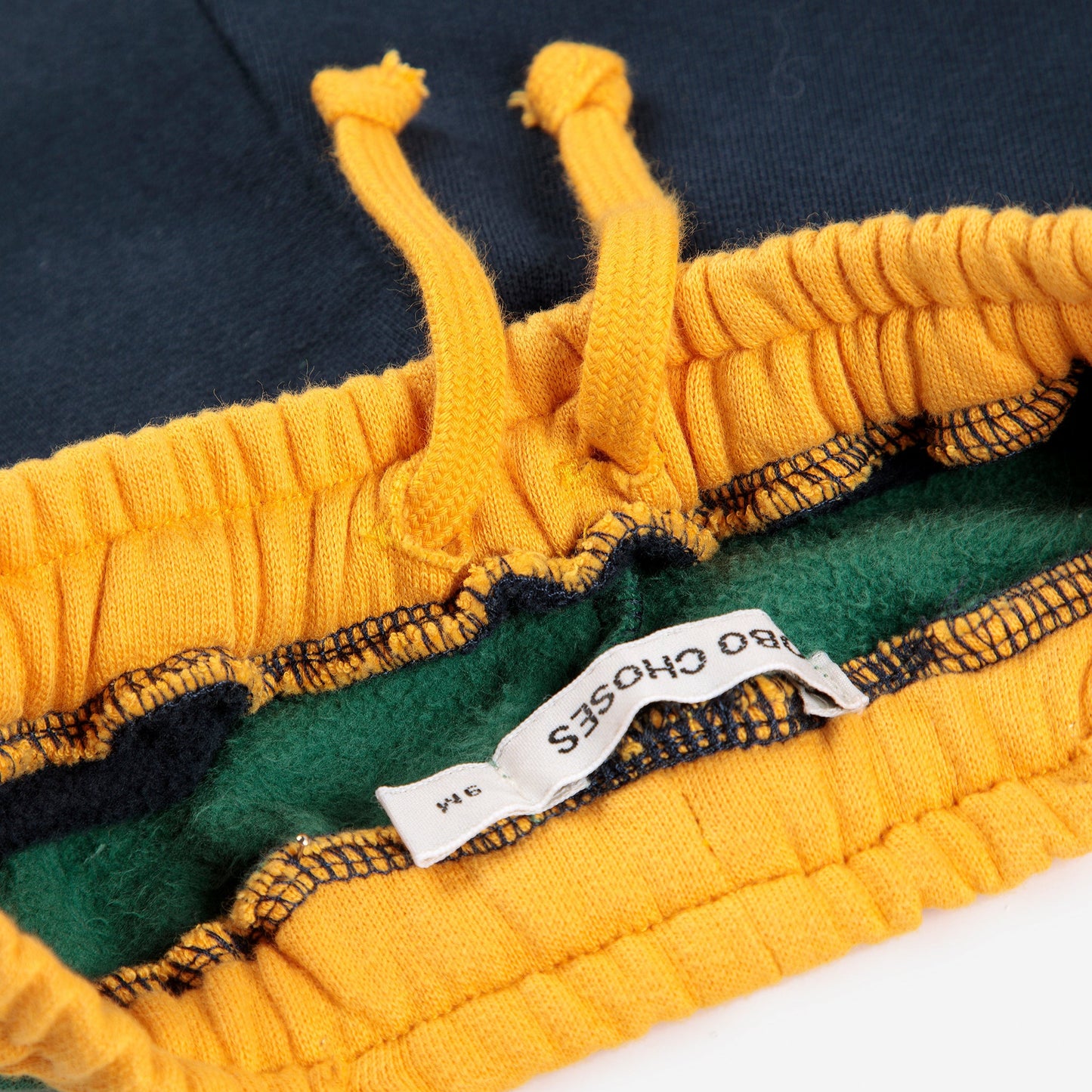 Close-up of a yellow and green fabric with a brand label on a white background