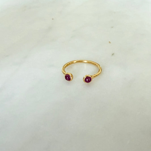 Gold ring with two red gemstones on a light gray background