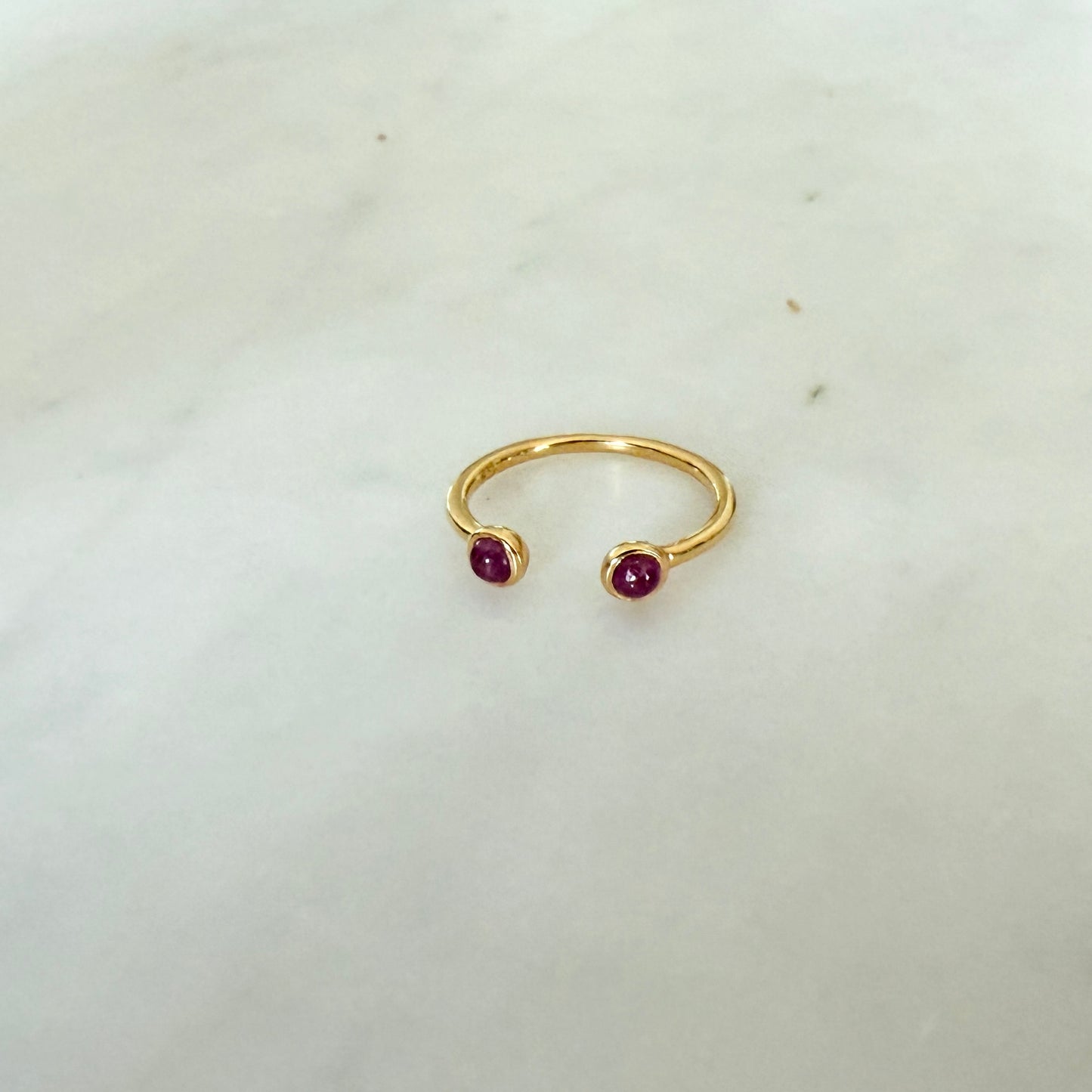 Gold ring with two red gemstones on a light gray background