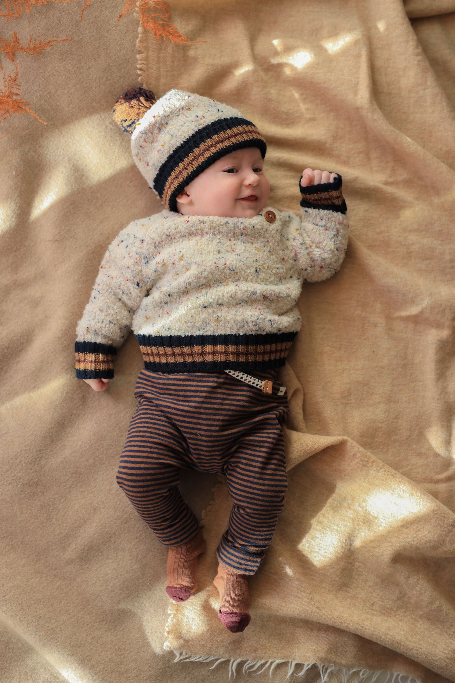 Baby wearing a striped sweater and hat lying on a beige blanket