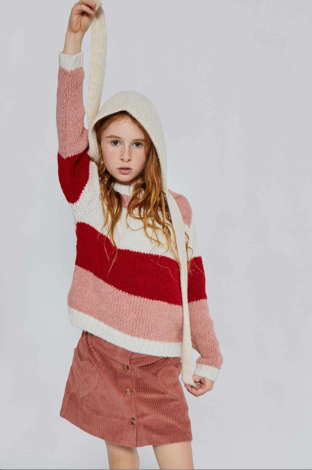 Person wearing a red and white striped sweater with a hood on a plain background