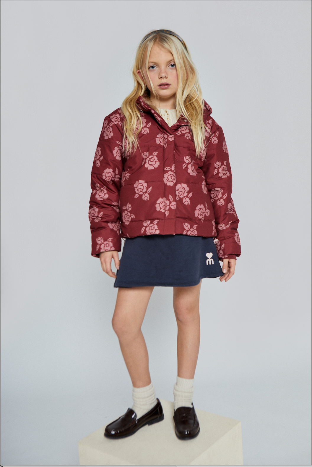 Young girl wearing a red floral puffer jacket with cross-stitch flower print