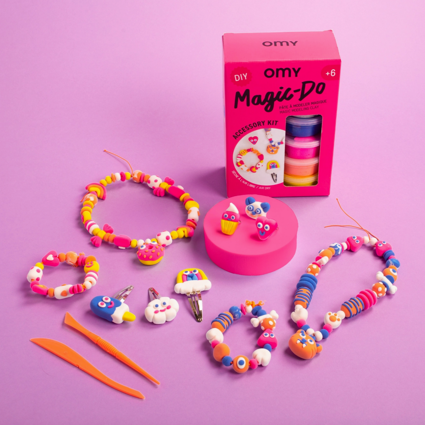 Colorful beaded bracelets and accessories with OMY packaging on a pink background
