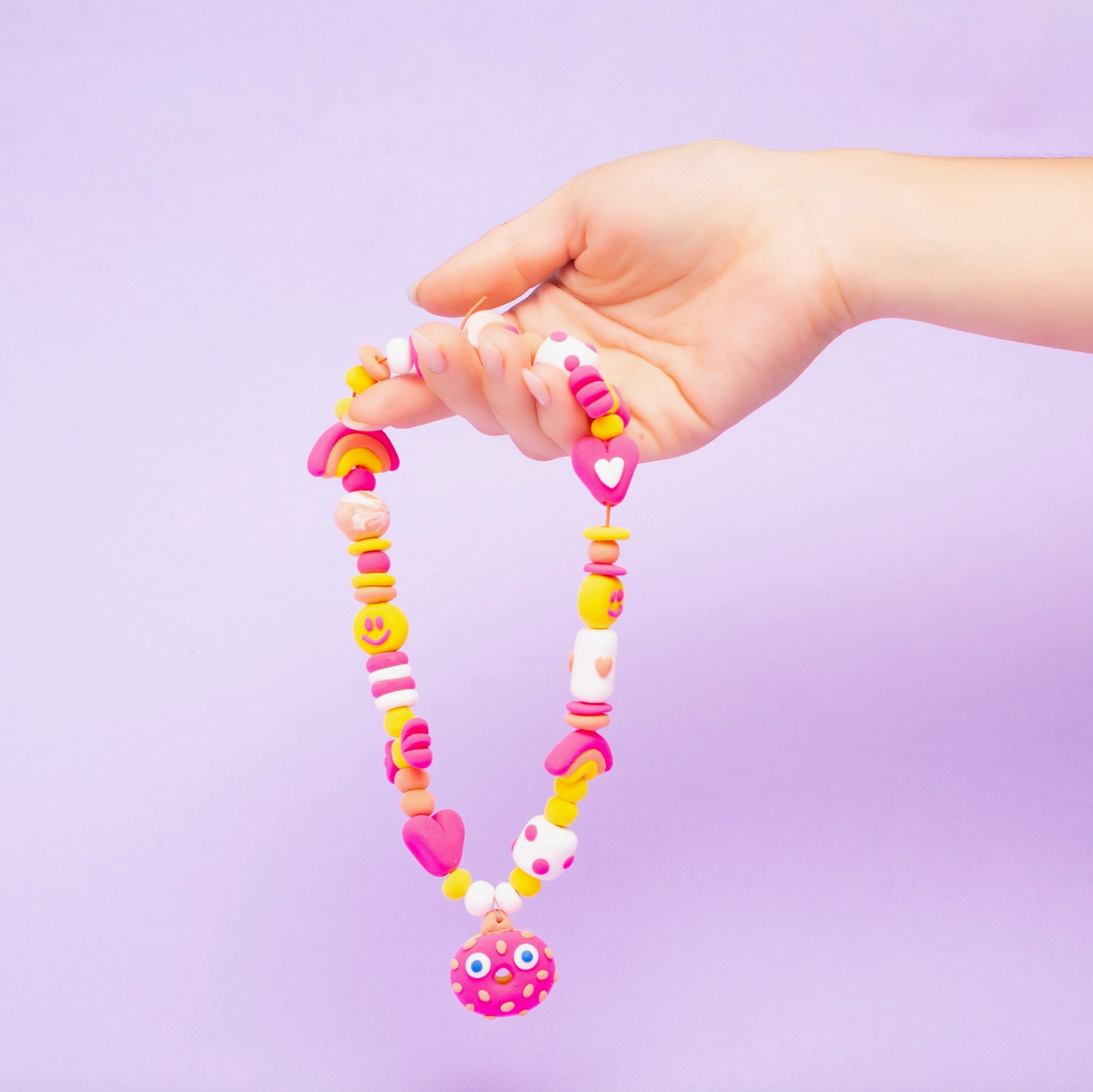 Hand holding a colorful necklace against a light purple background