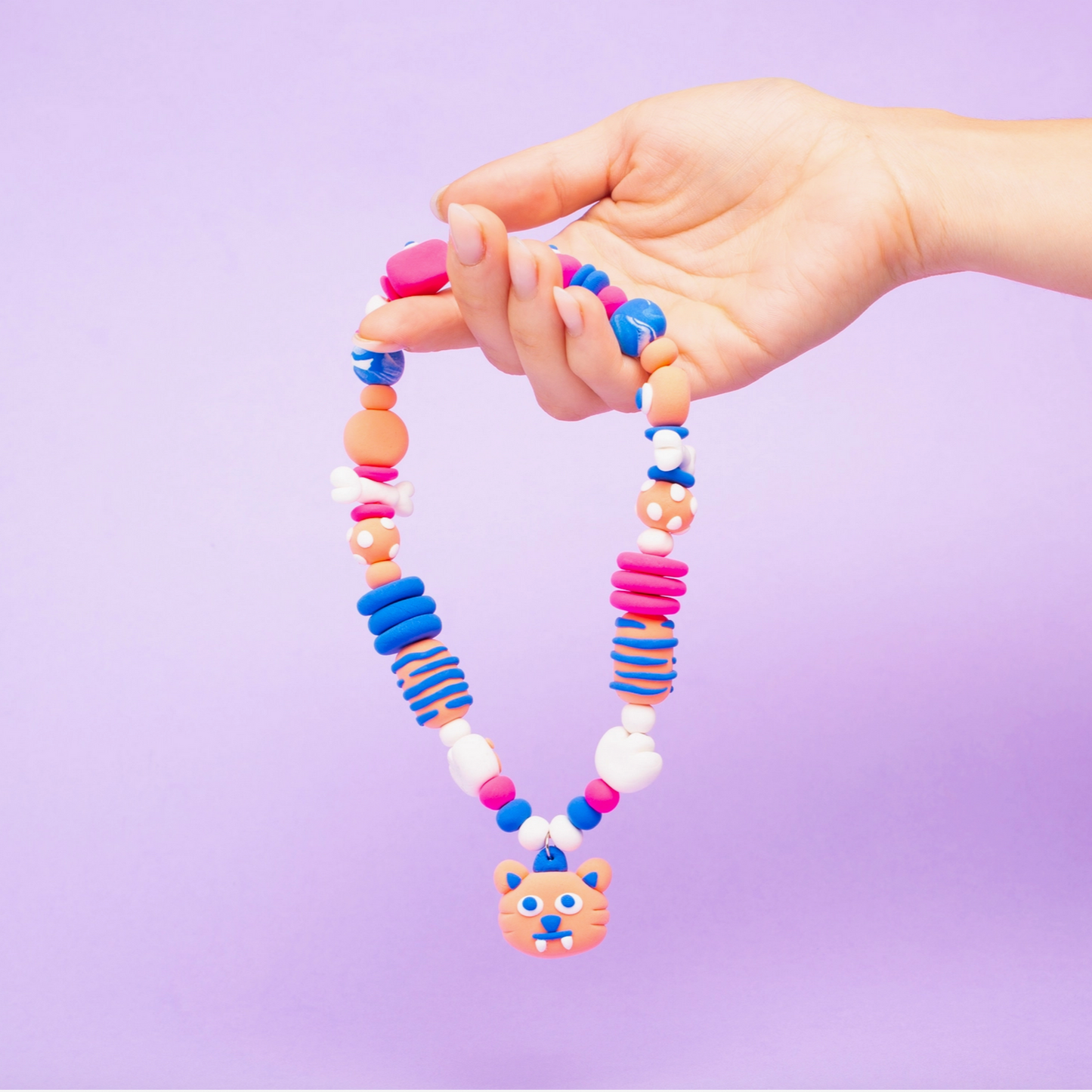 Colorful beaded necklace with a bear pendant held by a hand against a purple background