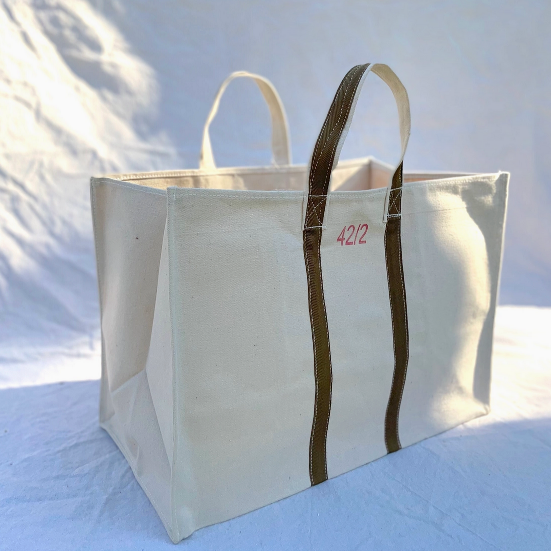 Large white tote bag with brown handles on a light blue background — Little-ish