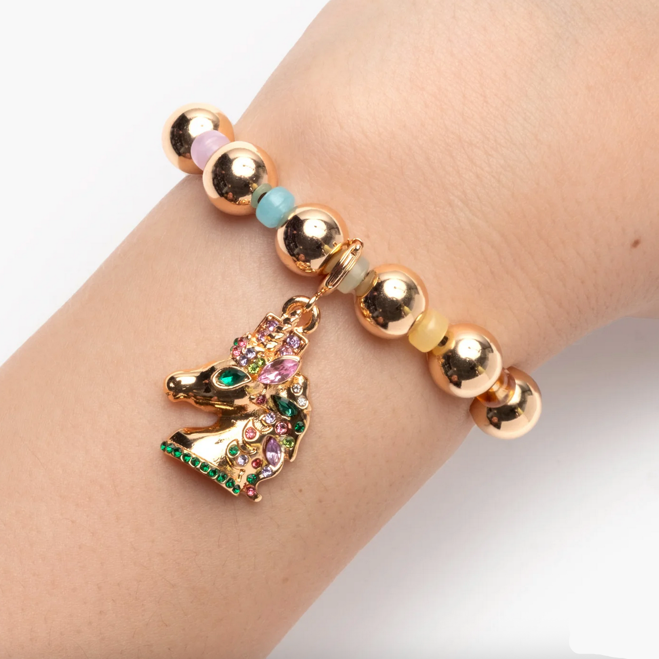 Bracelet with gold beads and a colorful unicorn charm on a wrist.
