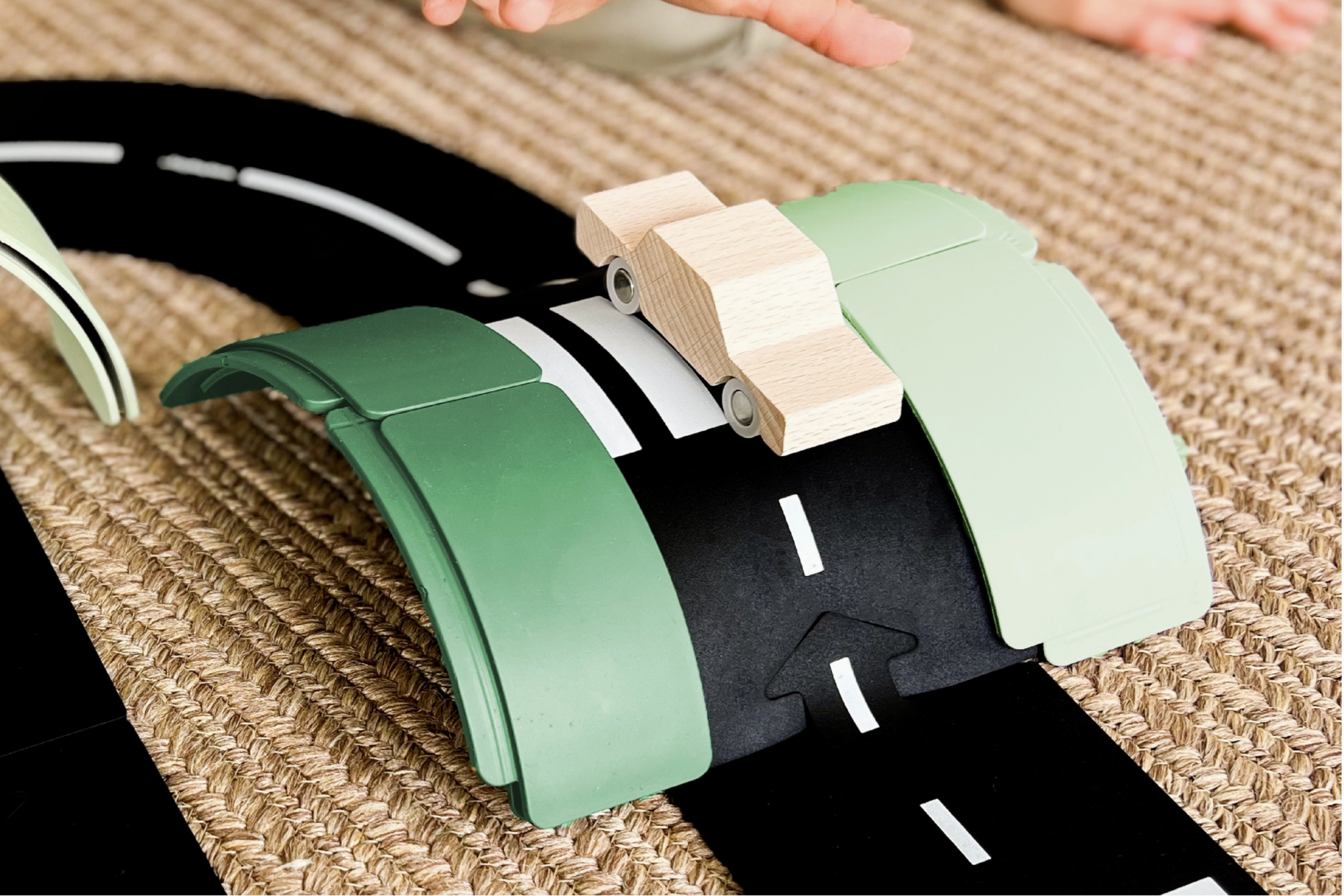 Toy road set with green and black roads and beige traffic cones on a textured surface.