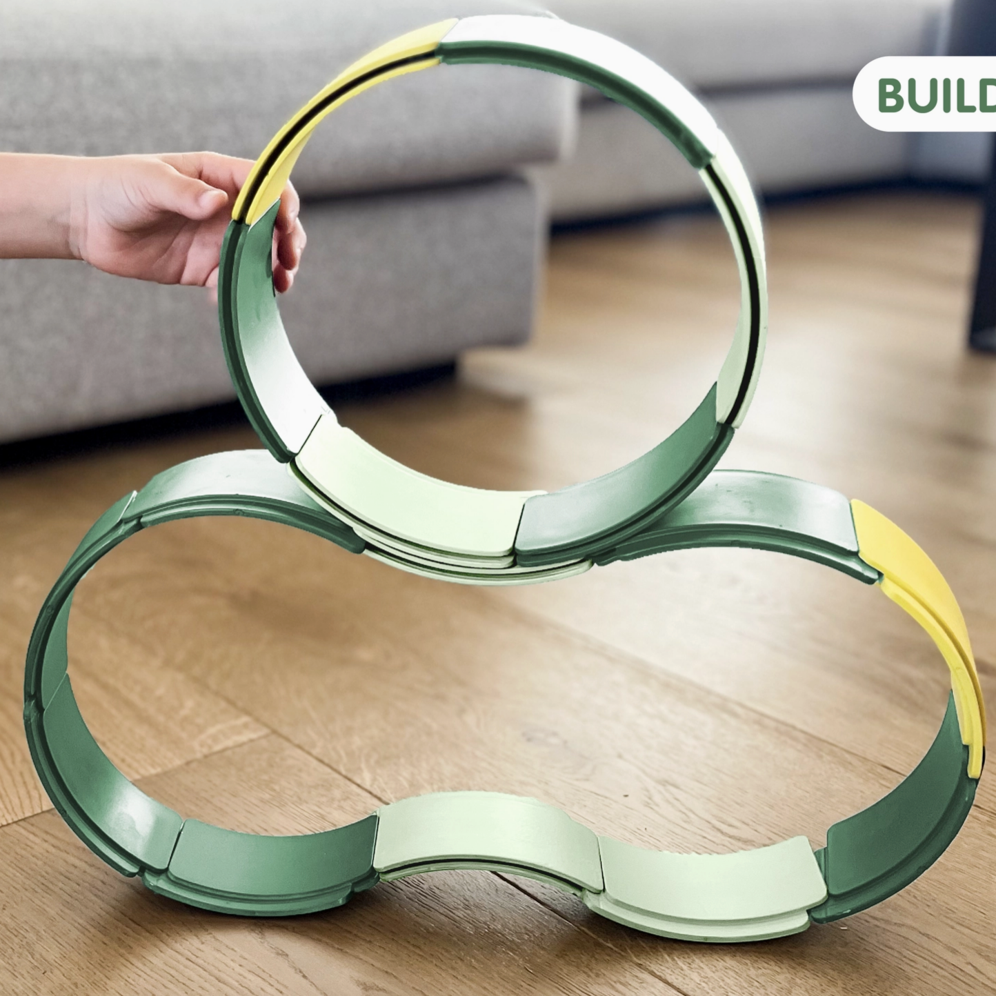 Children's toy made of interlocking rings on a wooden floor with 'Build & Play' text.