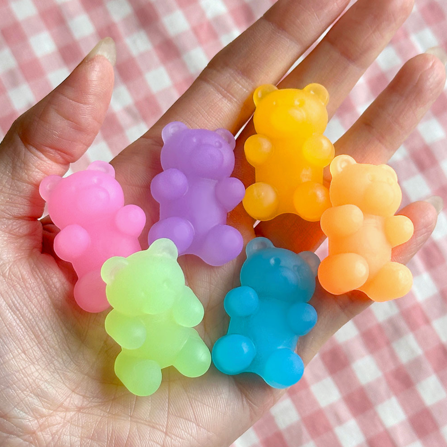 Colorful bear-shaped stress balls held in a hand against a checkered background