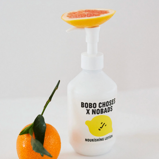 White lotion bottle with 'Bobo Choses x Nobads' branding next to a grapefruit on a light gray background