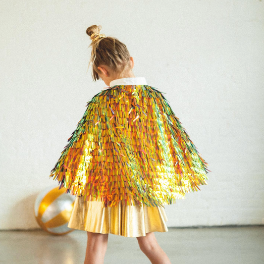 Child wearing a colorful sequin cape and gold skirt against a white background