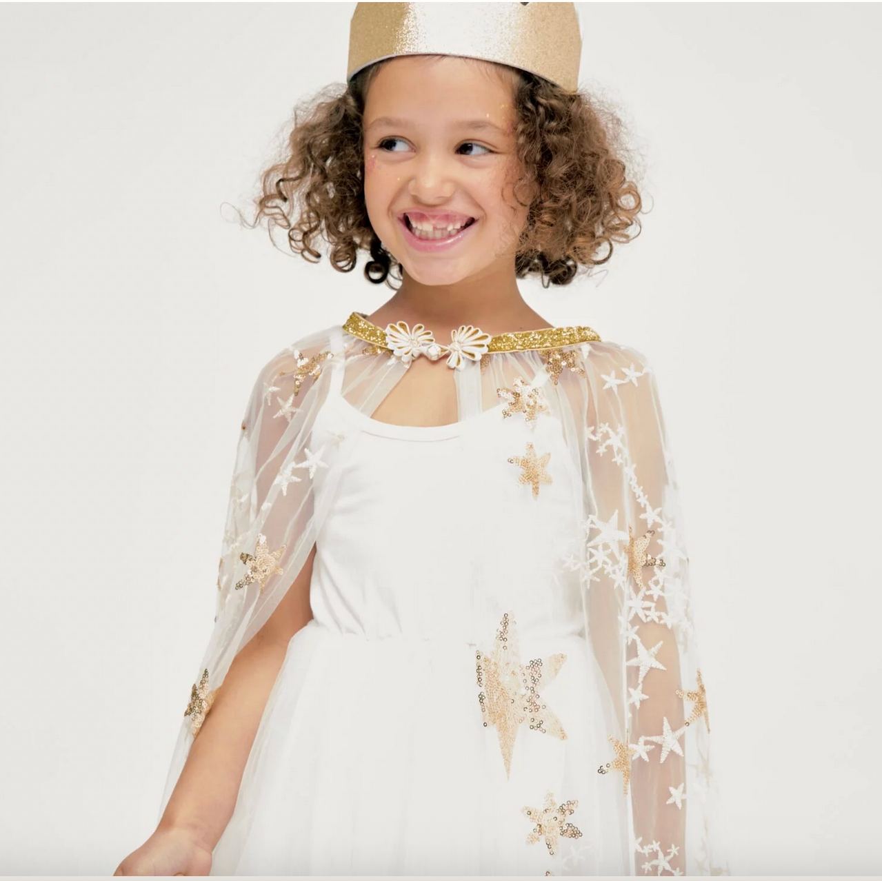 Child wearing a white dress with gold star designs and a matching headband on a white background