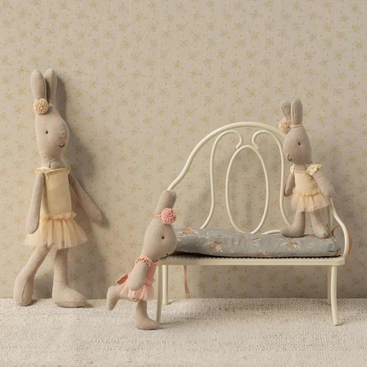 Three plush rabbit toys in a decorative setting with a bench and wallpaper.