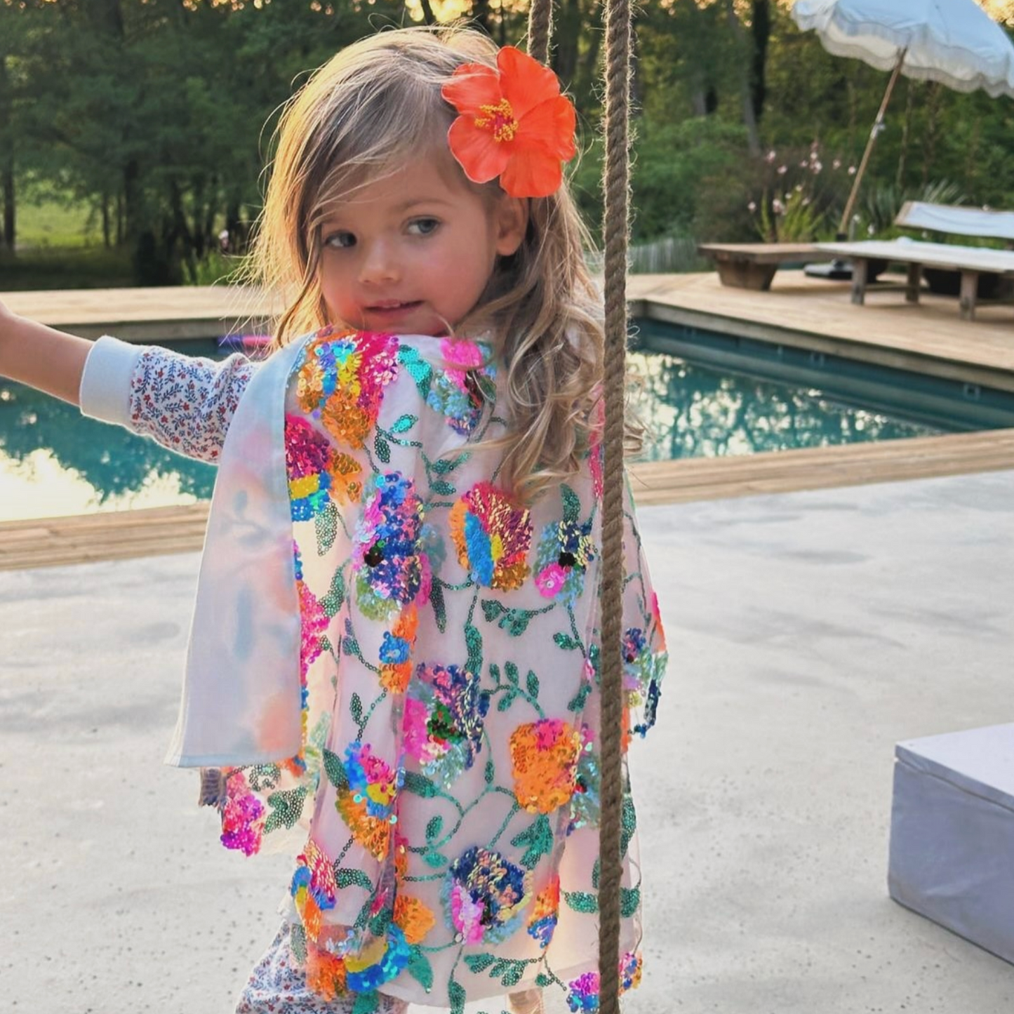 Young girl in a floral dress standing by a poolside
