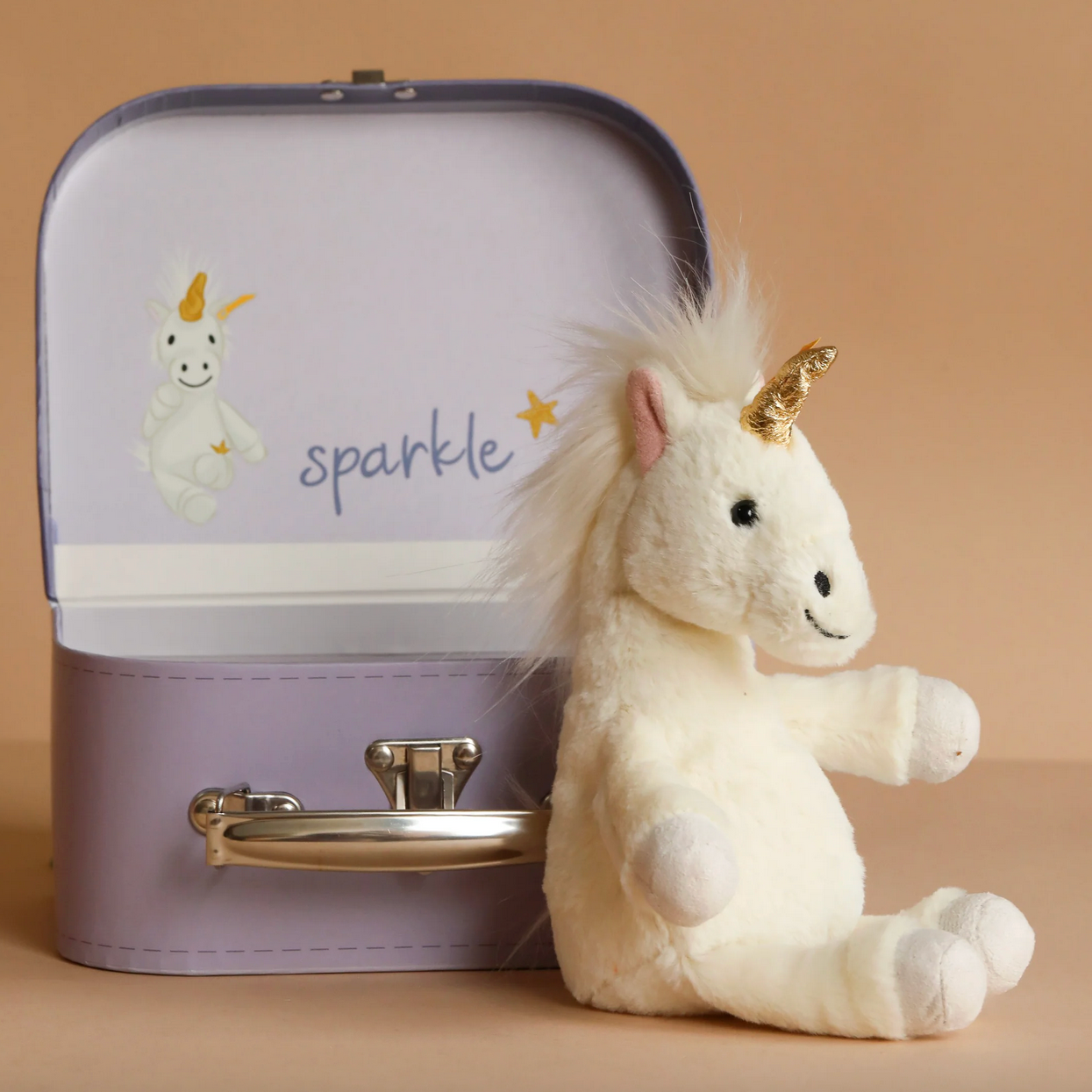 Plush unicorn toy with a suitcase labeled 'sparkle' on a beige background