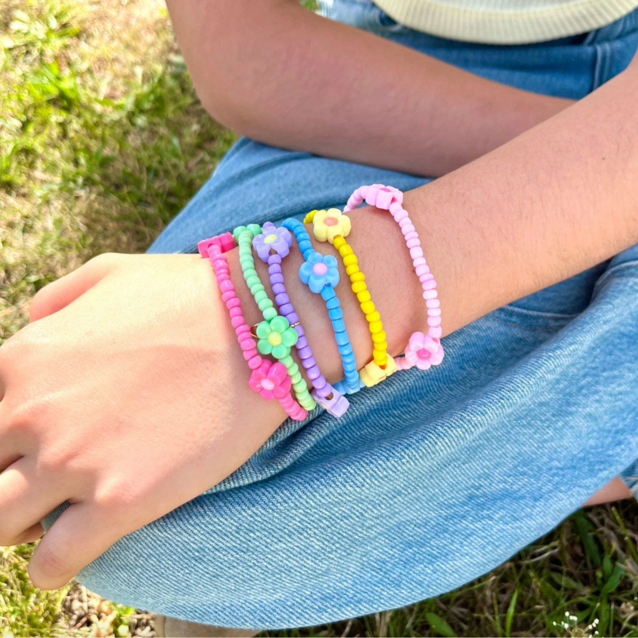 Colorful beaded bracelets on a child's wrist with a grassy background