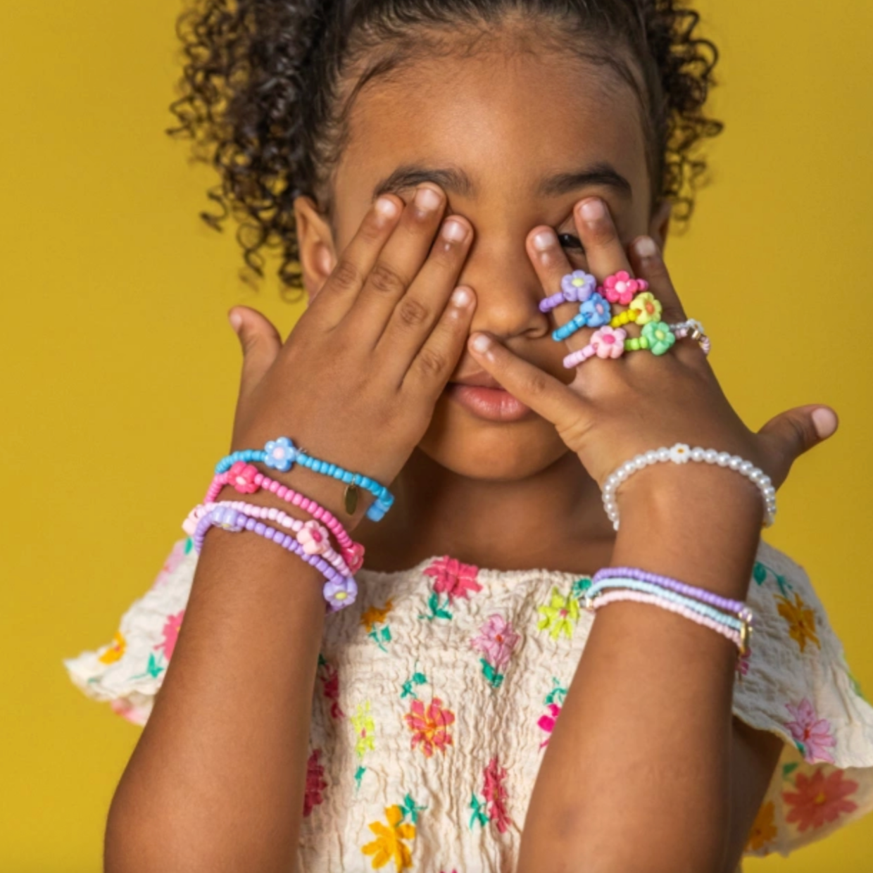 Child wearing colorful bracelets on a yellow background