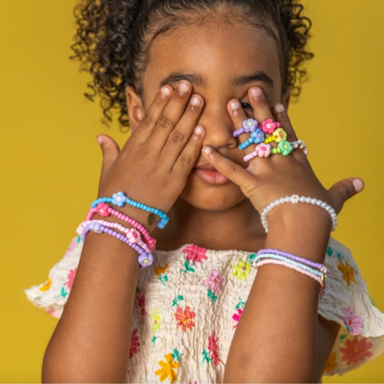 Child with colorful bracelets and rings on a yellow background